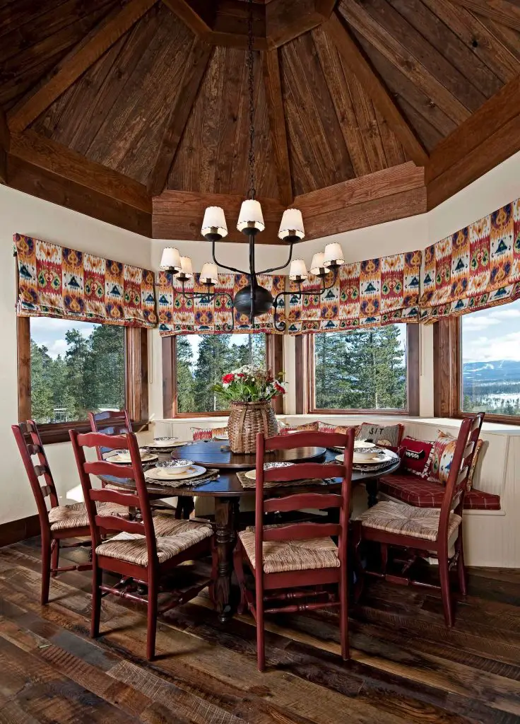 A Colorado breakfast nook with a pavilion style roof and dramatic views utilizes a curved banquette and an antique round table to create a roomy eating area