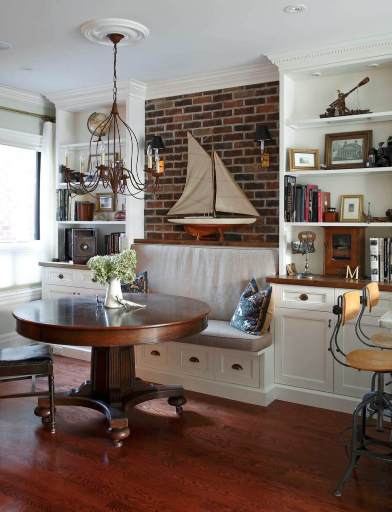 A brick wall featuring two black shaded sconces is the highlight of this nautical inspired kitchen banquette in Toronto