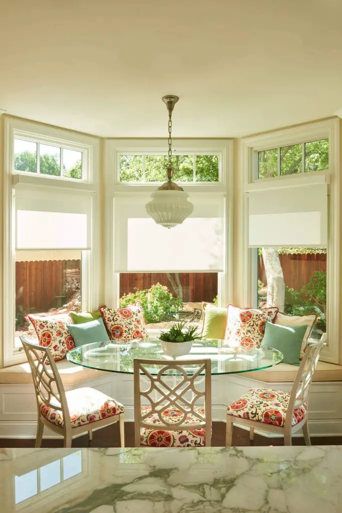 A curved banquette is paired with a glass top table and floral print chairs to make a bright and cheery breakfast area for a Los Angeles kitchen