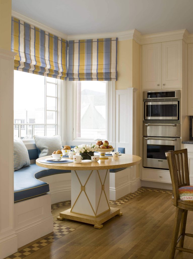 A rounded banquette covered in a light blue and gold trim is complemented by the similarly hued striped drapes found in this San Francisco kitchen