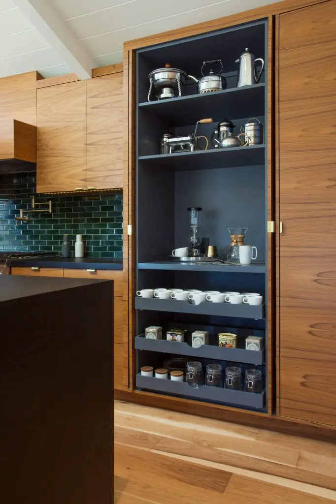 Lovely walnut cabinets in this midcentury modern kitchen open to reveal a dramatic black-painted coffee station with custom pullout drawers. Space was designed by Peninsula Modern.