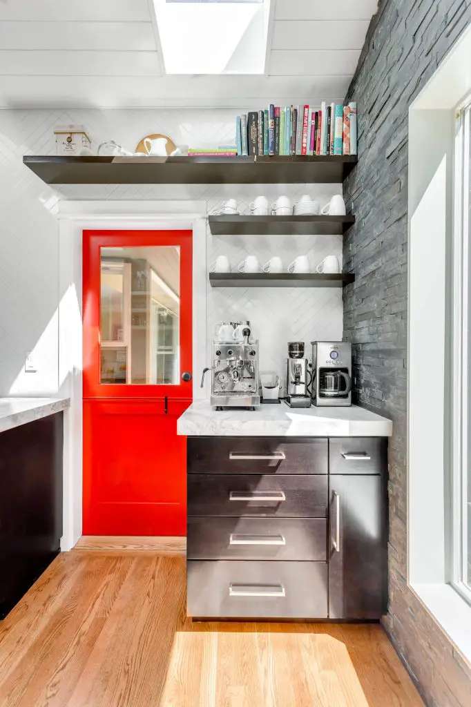 An espresso-stained cabinet with a marble top makes for a stylish coffee station to the right of the Dutch door in this Seattle kitchen by Design Harmony. A trio of floating shelves above the cabinet stores coffee cups and accessories.