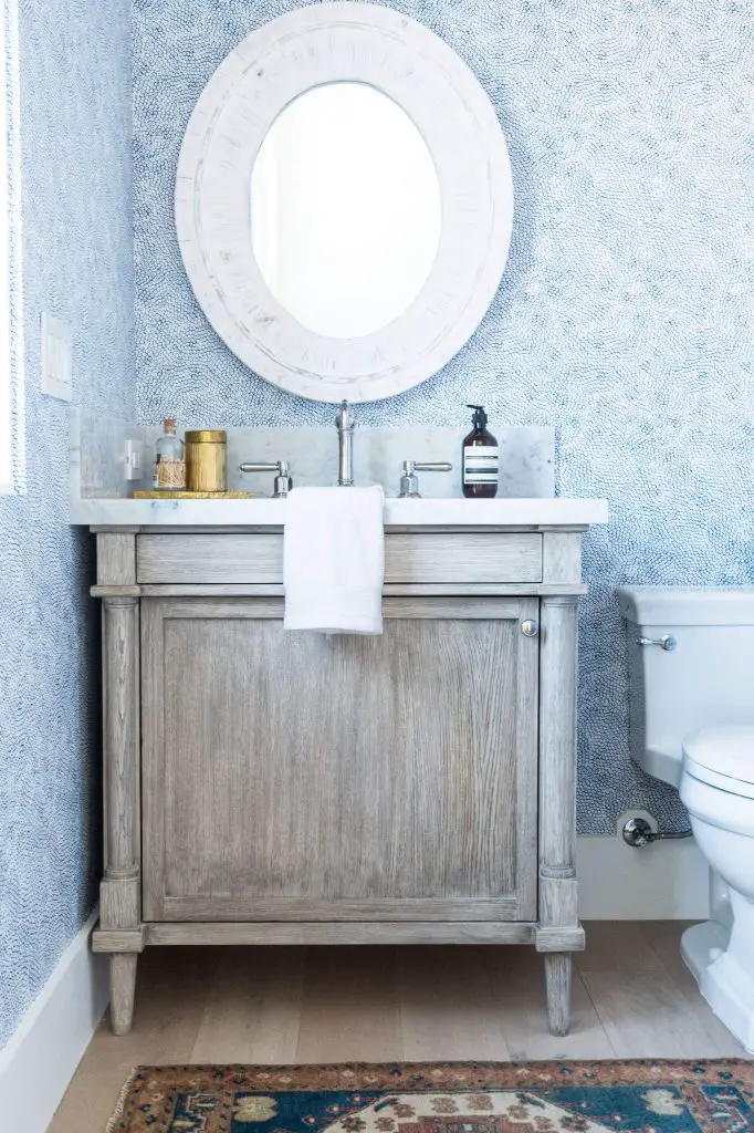 Designer Denise Morrison used a whitewashed mirror, blue wallpaper, and gray-washed oak vanity to help create this beach-inspired powder room in Orange County, California.