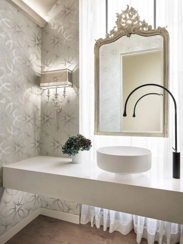 Duet Design Group cleverly hung a mirror in front of the window in this Denver powder room. A floor-to-ceiling linen curtain filters the natural light in this elegant space.