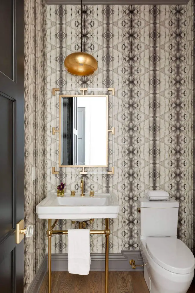An abstract wallpaper, a gilded pendant light, and a sink with brass legs are among the stars of this Minneapolis powder room designed by Kroiss Development.