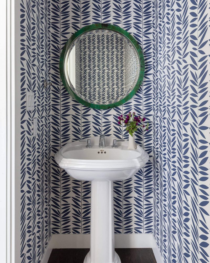 A round malachite mirror and whimsical wallpaper bring visual appeal to this San Francisco powder room designed by Kimberley Harrison Interiors.