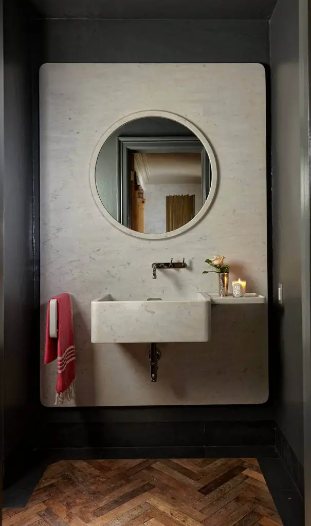 This Palm Beach, Florida, powder room built by Beacon Construction Group features a slab of marble attached to the back wall. A round mirror is recessed into the wall, and the vanity is made of the same marble, creating a unified look.