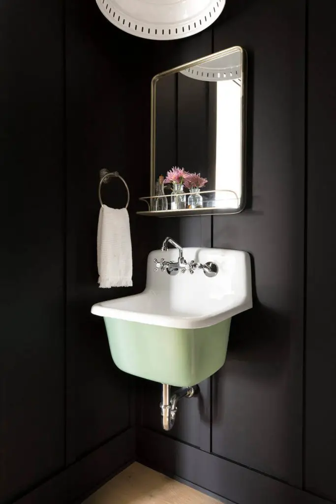 A vintage porcelain sink received a coat of mint-colored paint to make it pop against the black walls in this Minneapolis powder room by Sustainable Nine Design + Build.