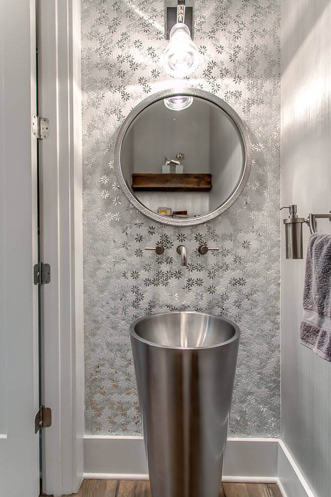 A large stainless steel vessel sink, a stainless steel soap dispenser hung on the wall and a round stainless steel mirror works well together in this Orange County, California, powder room by Design Design Interiors.