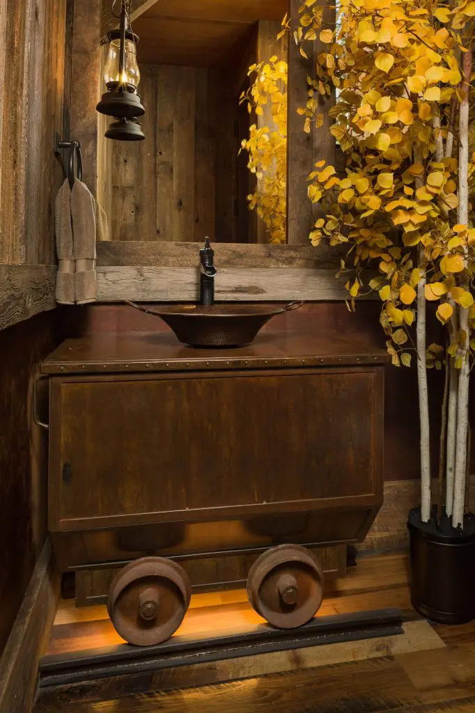 This rustic Colorado powder room features a vintage train cart transformed into a vanity that sits atop old train tracks. Space was built by Kogan Builders.