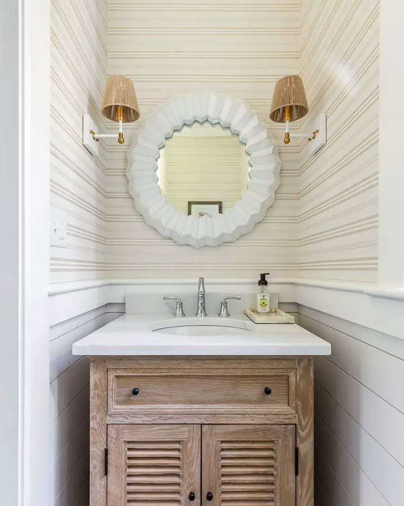 Cutting Edge Homes gave this Boston powder room a coastal vibe. Space features sconces with seagrass shades, a distressed-wood vanity, and white plank-covered walls.