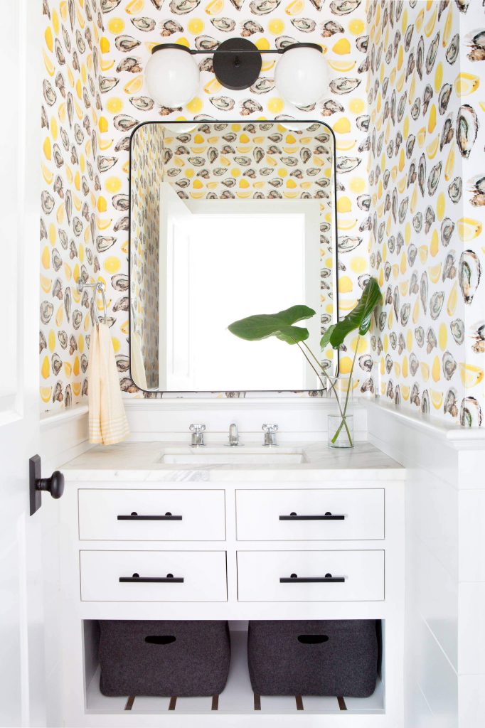 Beyond the stylish black fixtures and hardware and the whimsical wallpaper, note the two storage baskets at the bottom of the vanity. All of these elements make for a well-considered powder room designed by Chango & Co.