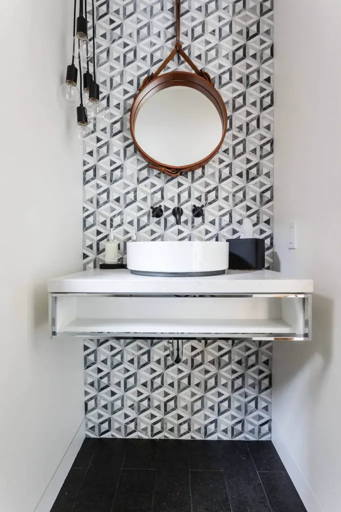 JMJ Studios combined a leather strap mirror, a cluster of exposed-bulb pendants, and black-and-white tile lining the back wall to create a stylish San Francisco powder room.
