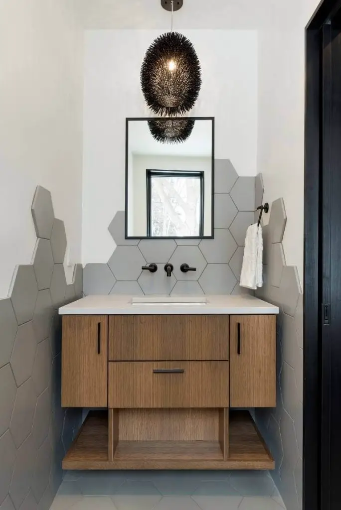 Walls covered unevenly in gray hexagonal tiles give this Minneapolis powder room. by Sustainable Nine Design + Build an artistic quality.