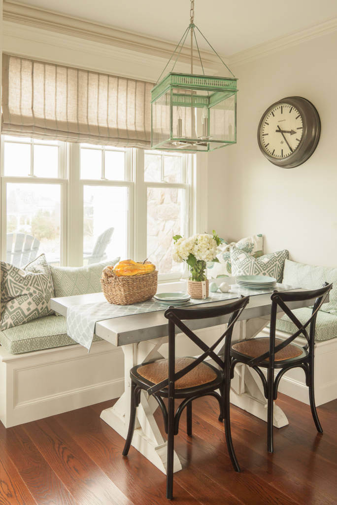 The mint green glass lantern pendant from The Urban Electric Co. blends well with the fabric covering the banquette in this Portland, Maine, beach inspired kitchen corner