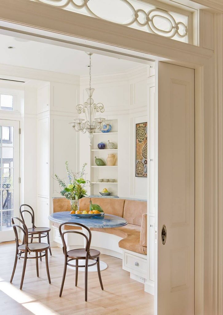 This traditional breakfast banquette in a Brooklyn Heights, New York, brownstone includes custom white cabinets constructed by Hemingway Custom Cabinetry and a smoky glass chandelier.