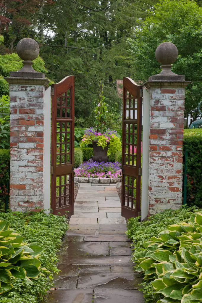 A combination of brick pillars and slatted wood gates welcomes guests down this garden path near Detroit, designed by Zaremba & Co.