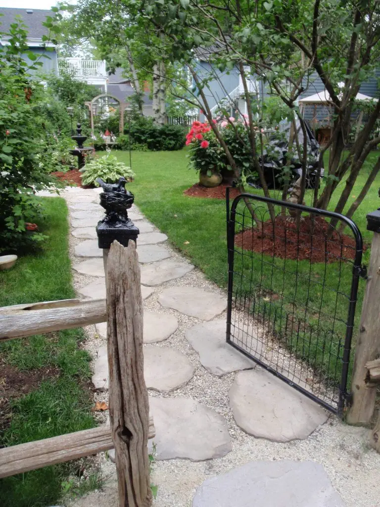 A fence made from driftwood and a black gate with a wire front provide a simple but elegant entry to this cottage garden in Toronto.