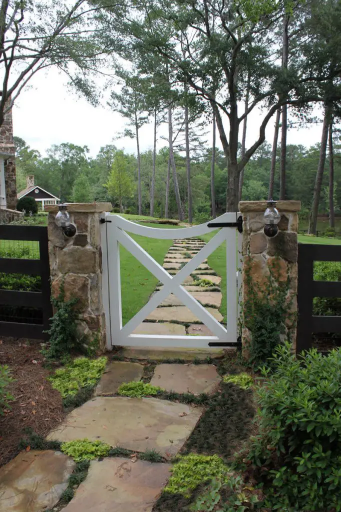 A horse fence, two brick pillars and an X shaped gate painted white lead to this Atlanta farmhouse property