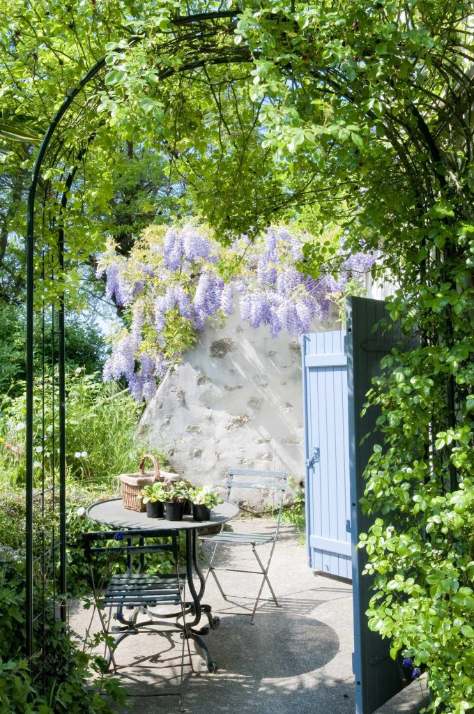 A metal arbor dripping in hanging vines creates an intimate garden entry for a country estate in France