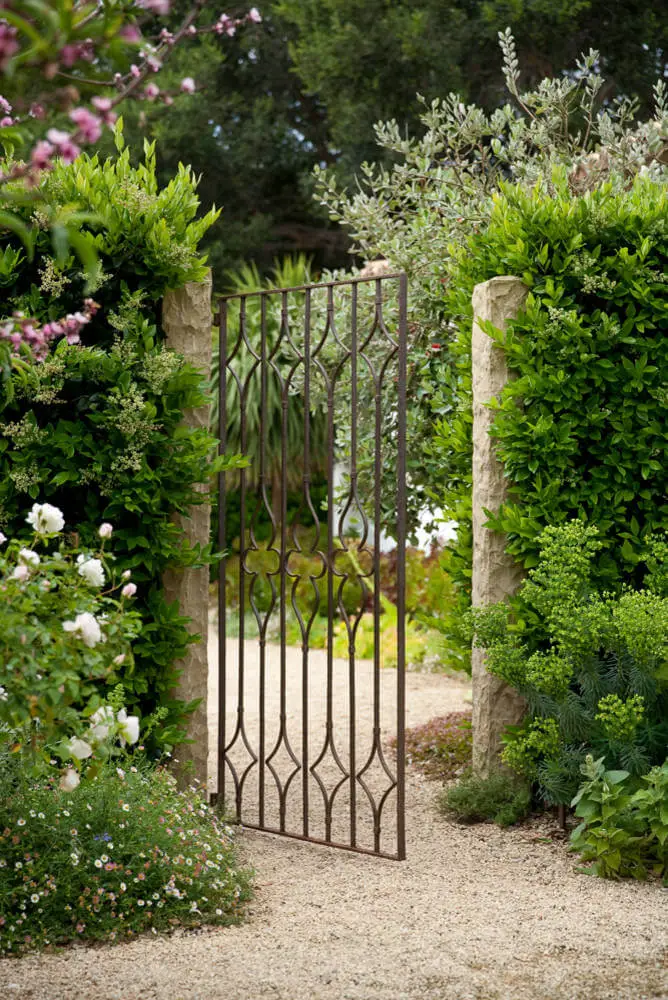 A thin iron gate provides an opening to this Mediterranean inspired garden in Santa Barbara