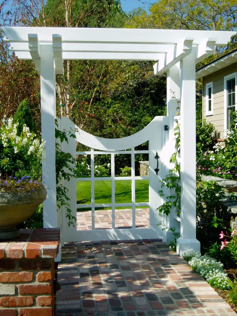 A white garden gate with a hanging iron lamp provides a stylish and well lit entrance