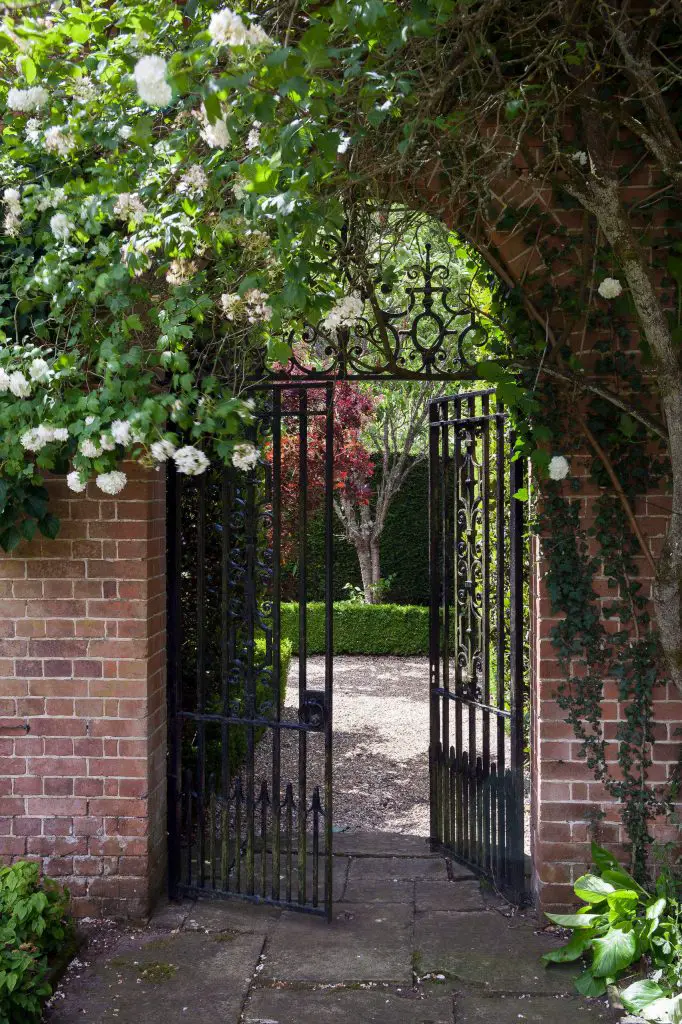 An iron gate with a coat of black paint breaks up the brick wall leading to this courtyard garden in England.