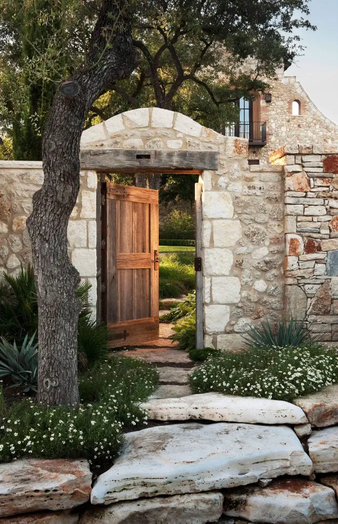 An open wood door leads to a series of covered spaces that invite visitors into a cobbled garden courtyard in Austin, Texas.
