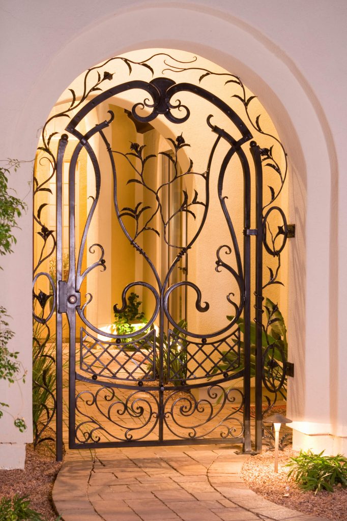 This garden courtyard gate, created by Grizzly Iron Inc., has many forged details, including calla lilies and leaves, scrollwork and a basket weave pattern.